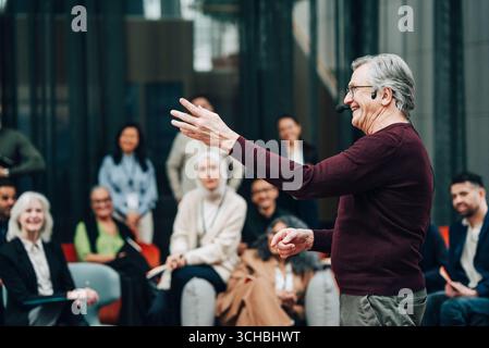 Happy male keynote speaker wearing headset gesturing while giving lecture at summit in convention center Stock Photo