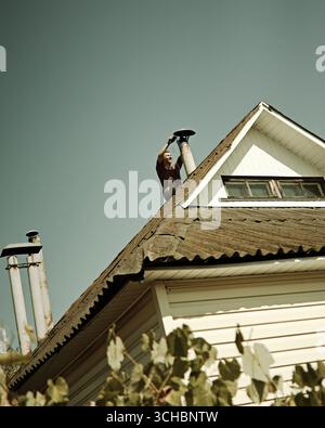 Man cleaning chimney on small rural house roof Stock Photo