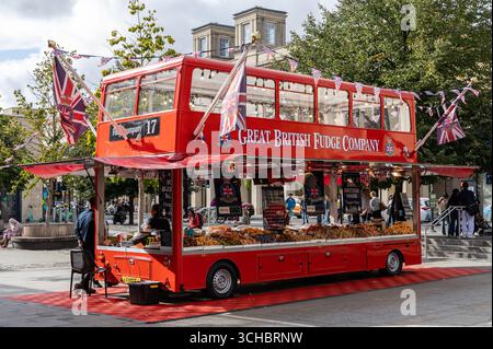 A vibrant red double-decker bus converted into a fudge shop by the Great British Fudge Company in a lively outdoor market setting Bath UK Stock Photo