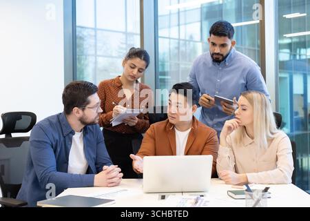 Five business professionals from diverse backgrounds gather around a laptop. Actively engaging in a collaborative discussion to analyze data. Strategi Stock Photo