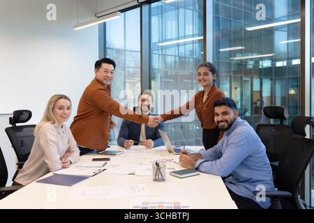 Diverse business team celebrating successful agreement, shaking hands after productive meeting in modern office boardroom, happy colleagues enjoying t Stock Photo