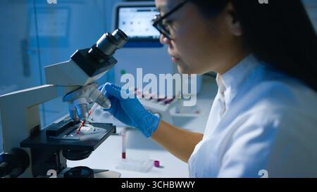 Woman scientist in a lab conducts research using a microscope, focusing on a sample in a controlled environment. Stock Photo