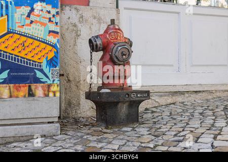 A weathered, bright red fire hydrant sits on a traditional cobblestone street in Lisbon. It's a colorful, functional detail of the city's urban landsc Stock Photo