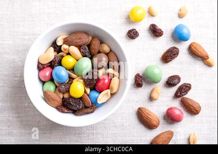 Rainbow trail mix in a white bowl on linen fabric. A snack mix of candy coated milk chocolate peanuts, roasted peanuts, raisins, and roasted almonds. Stock Photo