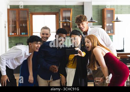 Taking group selfie, diverse teens smiling and celebrating together in school hallway, at home. Friendship, celebration, joy, technology, youth, toget Stock Photo