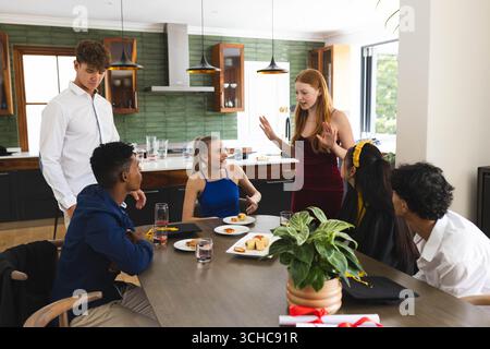 Diverse teenagers celebrating graduation at home, enjoying food and lively conversation. celebration, party, diverse friends Stock Photo