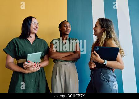 Smiling diverse female business professionals in smart casuals discussing against colorful wall in office Stock Photo