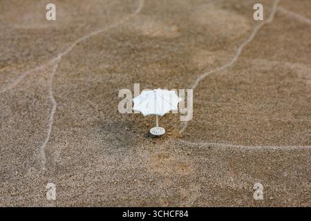 A miniature white parasol sits on textured sand, creating a simple yet captivating scene. A miniature white parasol stands on a sandy surface, possibl Stock Photo