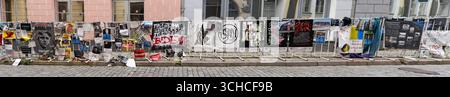 Panorama of Street art display with protest posters and graffiti on cobblestone street in historic European city center Stock Photo