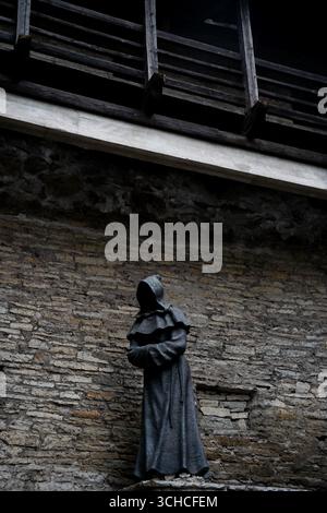 Medieval hooded figure statue against stone wall with wooden balcony in historic Tallinn Stock Photo
