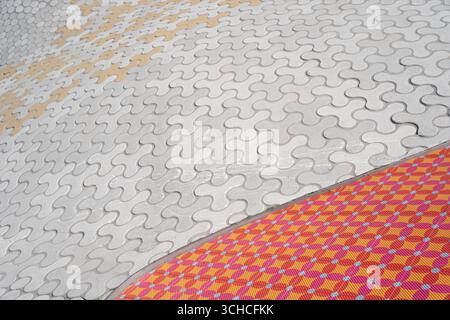 Distinctive wavy concrete pavement pattern meets colorful tiled surface in modern urban design Stock Photo