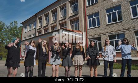 Diverse high school students waving hands, celebrating the end of the school year together outside their school Stock Photo