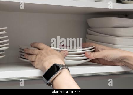 Housewife is putting a stack of square white plates on a kitchen shelf Stock Photo