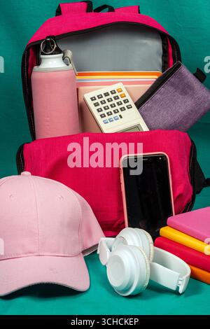 Pink backpack overflowing with school supplies on turquoise background Stock Photo