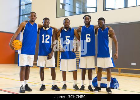 African American male basketball players in blue uniforms standing on court with basketball. Athletics, teamwork, leisure, sport, motivation, camarade Stock Photo