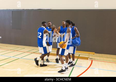 African American male basketball players high-fiving on court holding basketball and duffel bag. Athletics, teamwork, camaraderie, sportsmanship, comp Stock Photo