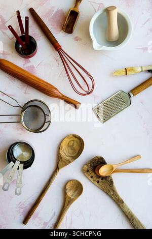 A flat lay collection of various rustic and modern baking utensils, including a whisk, rolling pin, grater, and wooden spoons, laid outp Stock Photo