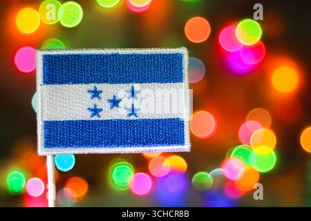 Embroidered Honduras flag with rainbow bokeh fireworks background, symbolizing Independence Day, New Year celebration, and patriotic pride. Stock Photo