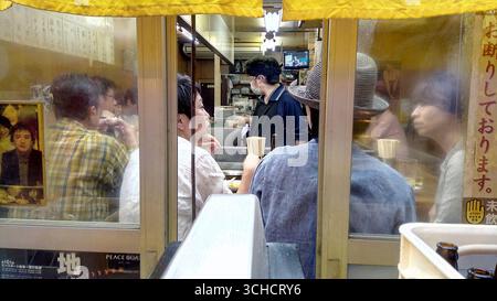 People eating inside a small, traditional Japanese eatery, viewed through a window on a rainy day. Stock Photo