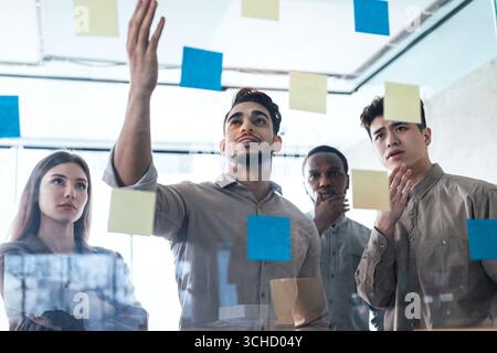Diverse colleagues brainstorming using sticky notes on glass wall Stock Photo