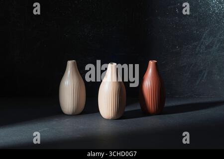 Three ceramic vases on black background in the light. Stock Photo