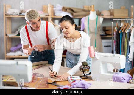 Female and male dressmakers drawing on paper in sewing studio Stock Photo