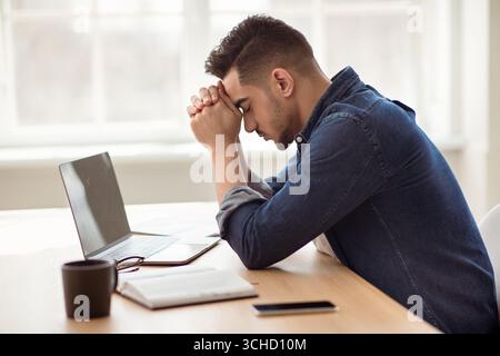 Depressed arab man sitting in front of laptop, office interior Stock Photo