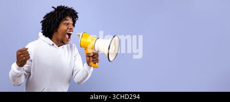 Emotional black adolescent shouting into megaphone, making announcement over violet studio background Stock Photo