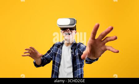 Excited young guy experiencing virtual reality in VR headset, making controlling gestures on orange background Stock Photo