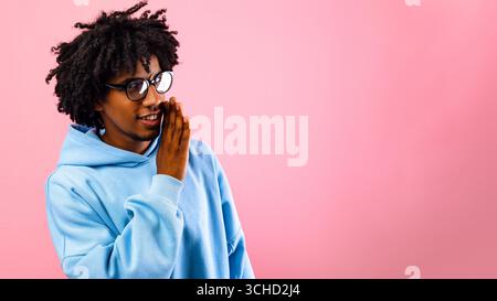 Portrait of black teenage guy whispering secret, sharing confidential information, spreading gossip on pink background Stock Photo