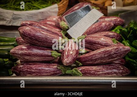 Close view of purple and white striped graffiti eggplants, also called Sicilian eggplants, stacked at a market stall beside other vegetables, highligh Stock Photo