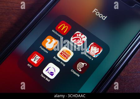 Mobile phone screen displaying a folder titled "Food" containing various fast food apps including McDonald's, Chick-fil-A, and Wendy’s. Stock Photo