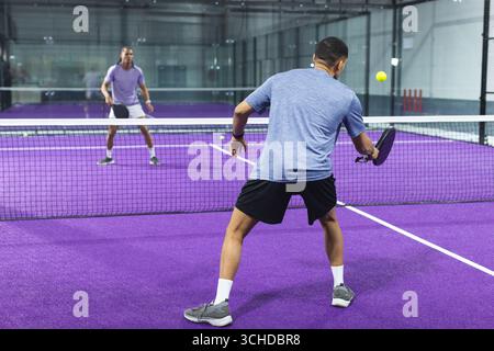 Two men in sportswear rallying ball over white net on purple court with paddles, copy space Stock Photo