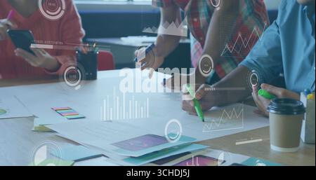 Collaborating professionals reviewing charts at meeting table in modern office, with data overlays Stock Photo