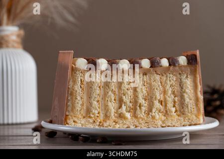 Close-up of a slice of chocolate layer cake with decorative chocolate pearls on a white plate against a blurred wooden background Stock Photo
