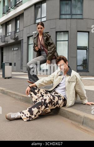 A young couple showcases their love while posing creatively on a city sidewalk under clear skies. Stock Photo