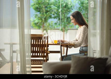 Happy woman using laptop sitting in a terrace in a house outdoors Stock Photo
