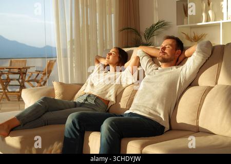 Relaxed couple resting sitting on a couch at home at sunset Stock Photo