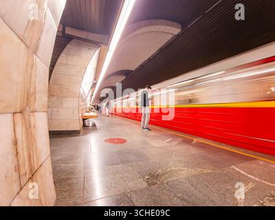 Commuter using mobile phone while standing on platform as high speed train arrives in Prague Metro station, showcasing urban transportation and modern Stock Photo