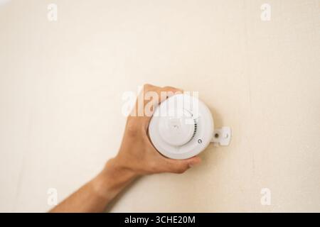 Close-up hands of unrecognizable electrician mounting smoke detector on wall, ensuring safety and protection of building by installing reliable fire Stock Photo