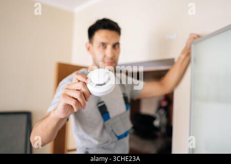 Selective focus portrait of blurred electrician holding smoke detector while installing in residential building, prioritizing fire safety and ensuring Stock Photo