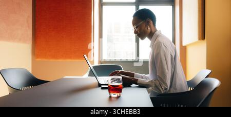 A focused person on a laptop at a modern desk in a naturally lit room with minimalistic decor, emphasizing productivity, business, and technology. Stock Photo