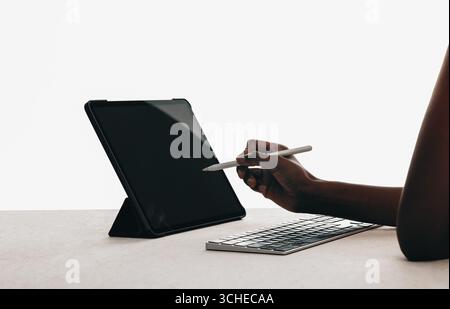 A closeup view of a person interacting with a digital tablet using a stylus. The workspace includes a keyboard and is minimalistic, emphasizing techno Stock Photo