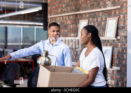 Diverse colleagues in office discussing while unpacking box, collaborating on project Stock Photo