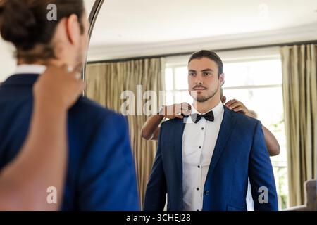 Wedding suits, male friends adjusting bow tie and blue suit in dressing room, with mirror reflection Stock Photo