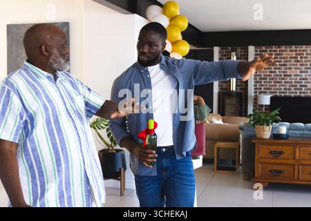 Two men in casual attire discussing while holding wine bottle at home Stock Photo
