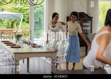 Women joyfully preparing dining table for wedding celebration at elegant venue Stock Photo