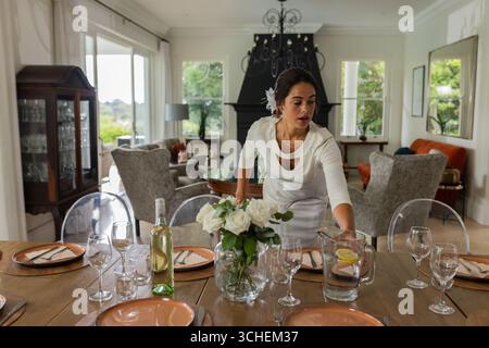 Woman in white dress setting elegant dining table with flowers and wine Stock Photo