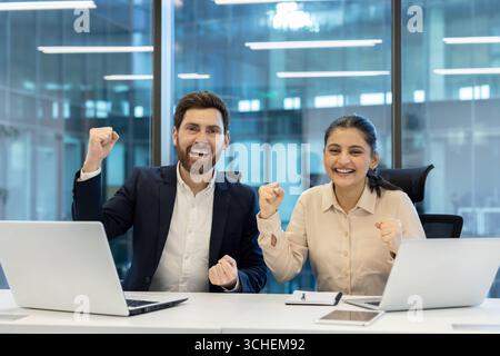 Two happy business colleagues are raising their fists in a modern office, expressing their excitement and joy over a successful project or achievement Stock Photo
