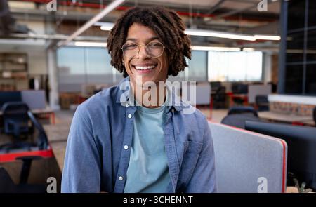 Smiling young man in modern office, enjoying creative work environment, copy space Stock Photo